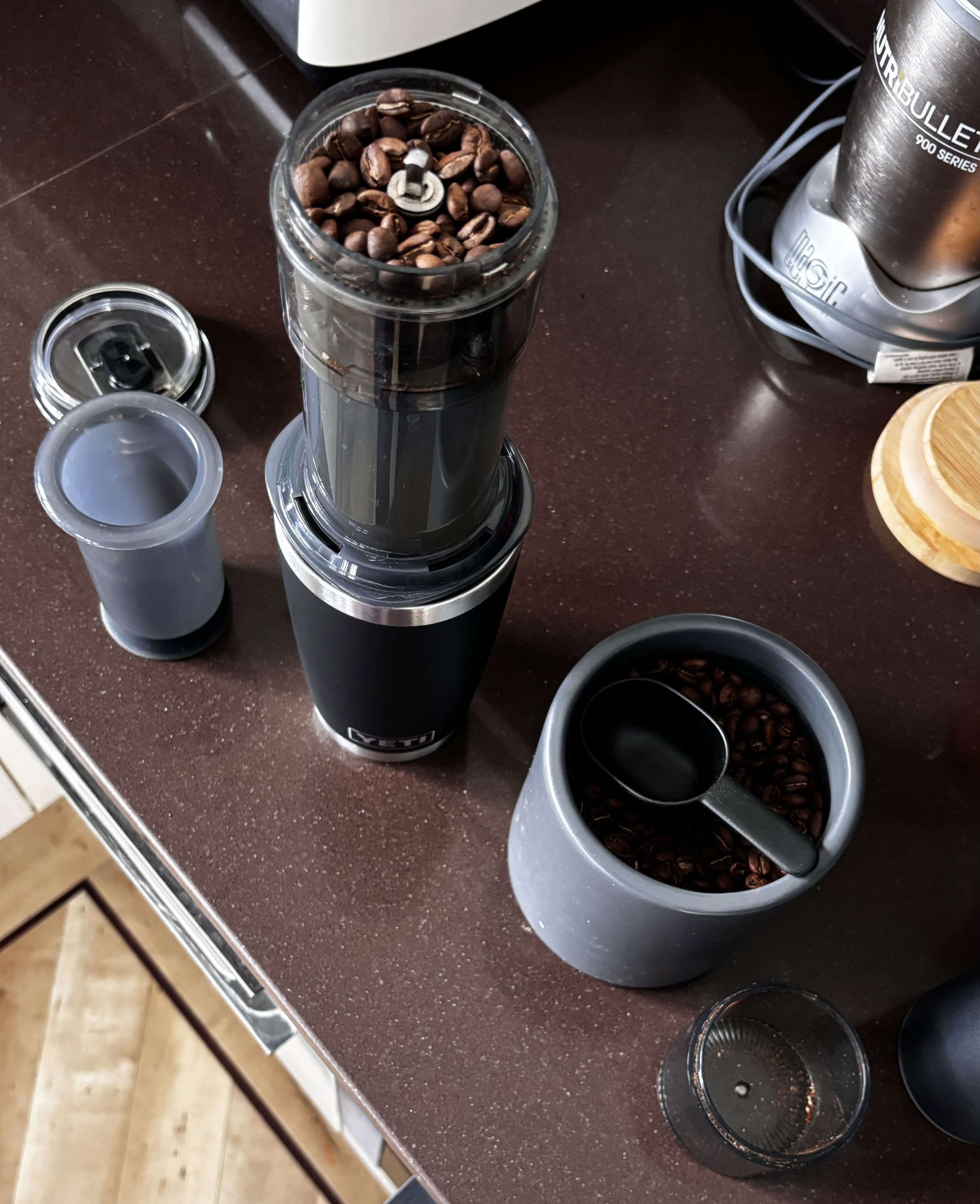 Step one. A photograph of a kitchen counter top. There&#39;s a Yeti cup, topped with an AeroPress, and then a circular plastic container filled with whole coffee beans. Next to it is a jar of whole coffee beans and a spoon.